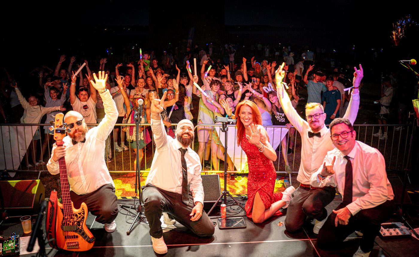 The Good Times on stage with arms raised in front of a packed festival crowd