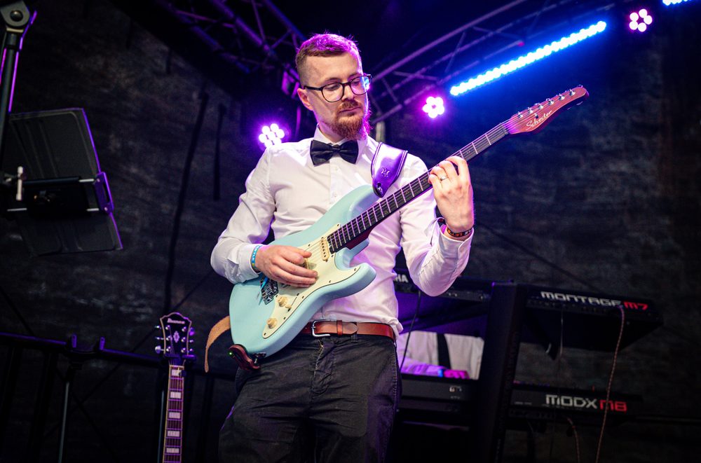 Lanni playing a light blue guitar under purple stage lights